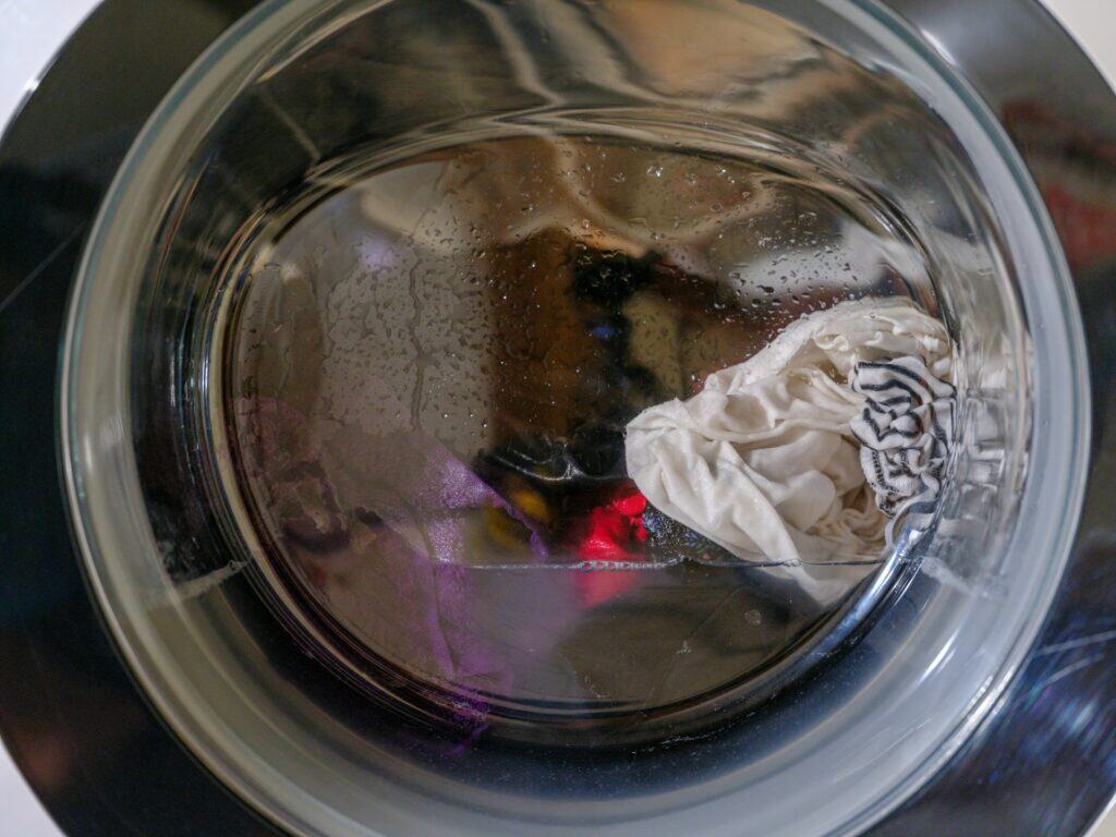 滾筒洗衣機玻璃門的近距離特寫,門上布滿細小水滴,內部可以看到正在攪拌洗滌中的深色與淺色衣物。