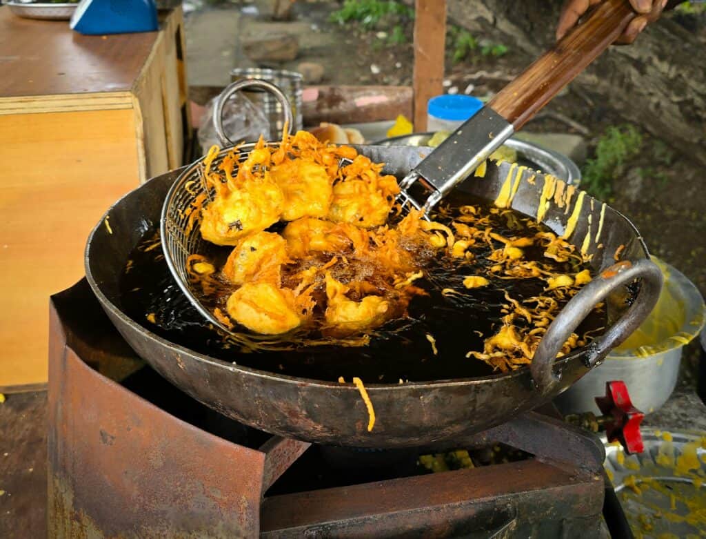 戶外攤販使用大鐵鍋油炸食物，油色深沉，鍋邊沾附黃色麵衣殘渣與黑色燻黑油跡。
