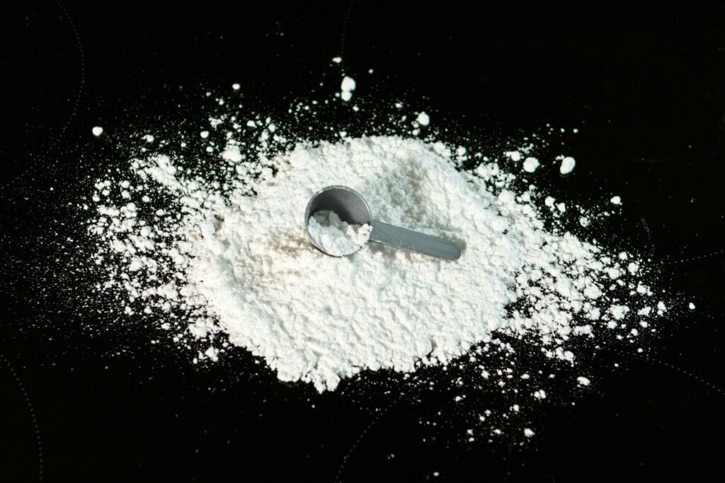 黑色背景上散開的細緻白色過碳酸鈉粉末,中心處放著一支盛滿白色粉末的深灰色圓形塑膠量勺。