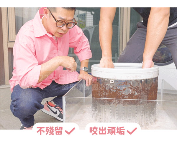 一名穿著粉紅色襯衫、戴著黑框眼鏡的男子，正在仔細觀察一個透明壓克力水箱內被清洗的洗衣機內槽。另一個人的雙手正握著內槽，水中充滿被洗出的深褐色污垢碎片。圖片下方帶有「不殘留」與「咬出頑垢」並打紅色勾勾的文字說明，展示洗衣機清洗的實際效果。